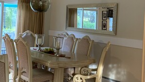 A dining room with a round table, ornate chairs, a chandelier, a ceiling fan, and a large mirror above the table.
