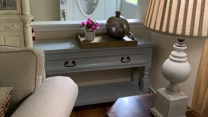 A living room with a white door, a green wreath, a vase with pink flowers, a lamp, and a wooden table with coasters.