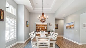 A dining area with a chandelier, white chairs, a wooden table, and a patterned rug.