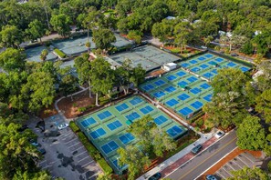 Luchtbeeld van een sportcomplex met verschillende tennisbanen, omringd door bomen en parkeerplaatsen.