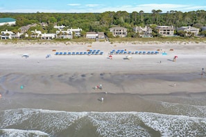 A beach with umbrellas and beachgoers, a sandy shore, and houses in the background.