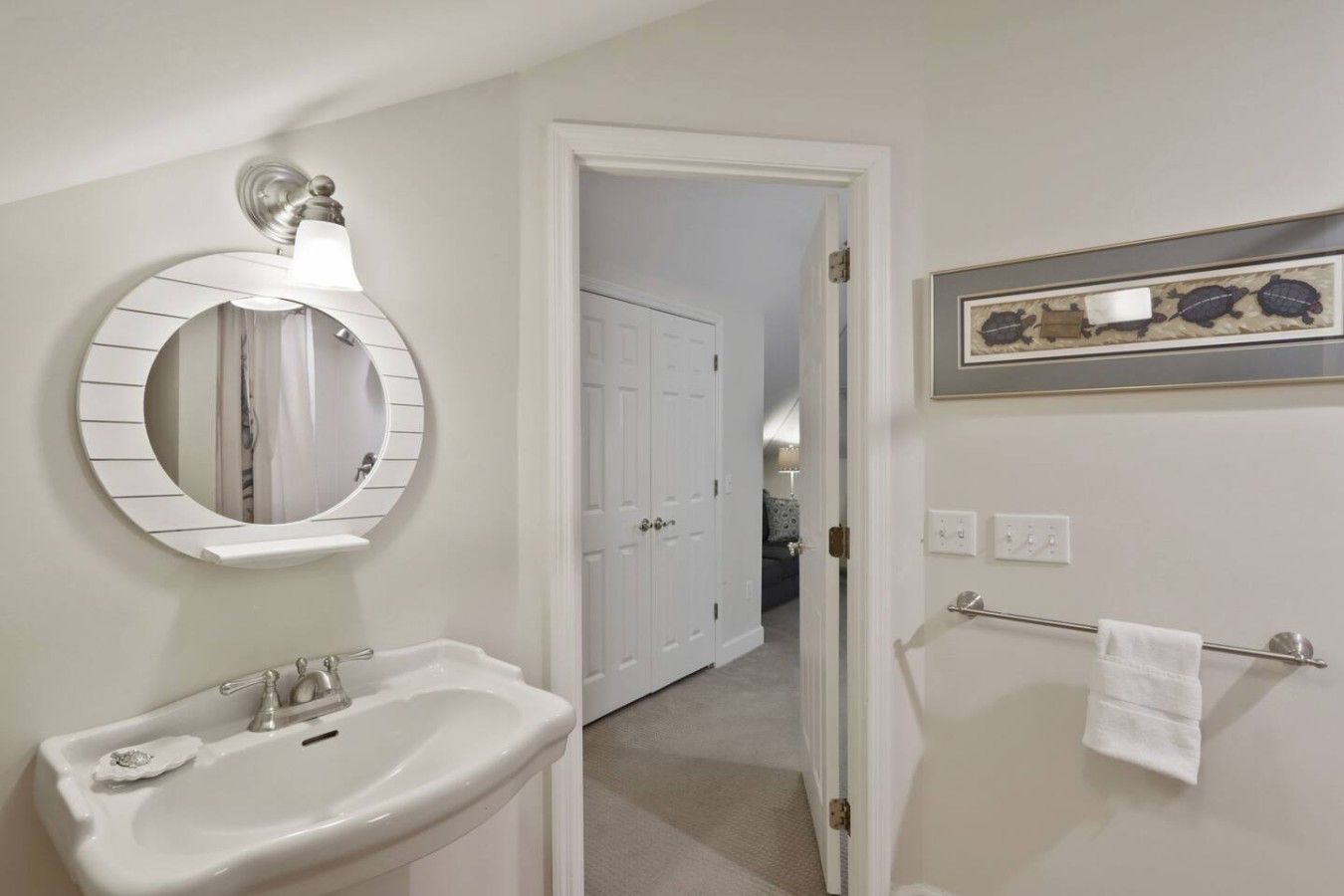 A bathroom with a round mirror, a sink, a towel rack, and a framed picture on the wall.