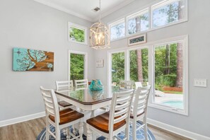 A dining area with a glass table surrounded by white chairs, a pendant light, and a view of a swimming pool.
