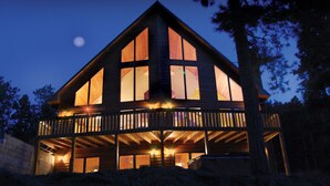 Une cabane en bois à deux étages, dotée d’un balcon, de grandes fenêtres et d’un escalier apparent.