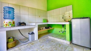 A compact kitchen with white cabinets, a gas stove, a water dispenser, and a refrigerator. - Kirana Homestay - Leaf Bungalow (Karangasem)