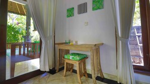 A room with a wooden table and a green cushioned stool, white curtains, and a view of greenery outside. - Kirana Homestay - Leaf Bungalow (Karangasem)