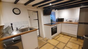 A compact kitchen with white cabinets, a microwave, a sink, and a dishwasher. - Cottage with Large Drive (Wiltshire)
