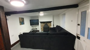 A living room with a black sofa, a stone fireplace, a television, and a door with frosted glass panels. - Cottage with Large Drive (Wiltshire)