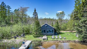 Une cabane avec un quai s’avançant dans un lac paisible, entourée d’une forêt dense.