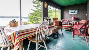 Un coin repas accueillant avec vue sur un lac, comprenant des chaises en osier, une nappe à rayures et une table en bois.