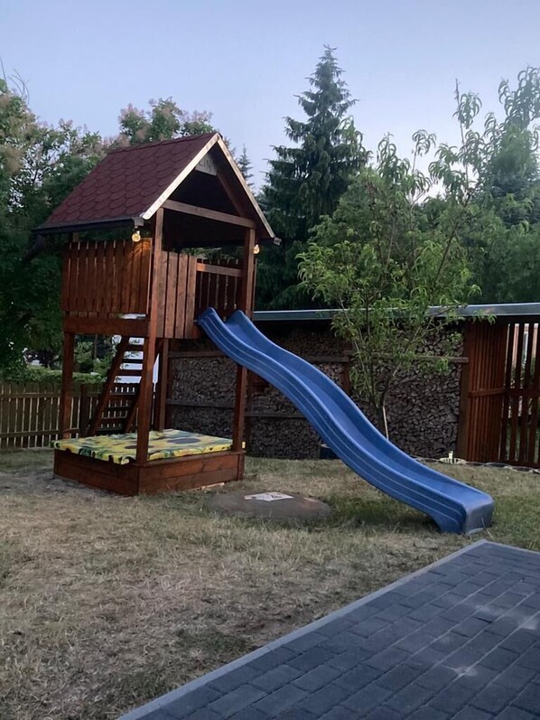 A wooden playhouse with a red roof and a blue slide. - Urlaub in der Natur (Godendorf)