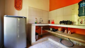 Une cuisine compacte équipée d’un réfrigérateur, d’un évier et d’un petit plan de travail sur lequel sont disposés divers objets.