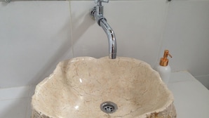 Une salle de bain dotée d’un grand lavabo en pierre de forme ovale, d’un robinet chromé et d’un petit robinet en cuivre.