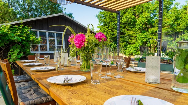An outdoor wooden table set for dining with chairs, a pergola overhead, and a house in the background. - Lots of space for large families (Neusalza-Spremberg)