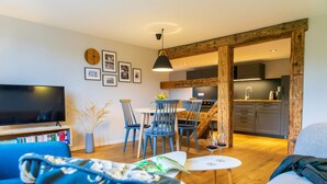 A modern living room with a flat-screen TV, a sofa, a dining area with chairs, and a kitchen in the background. - Lots of space for large families (Neusalza-Spremberg)