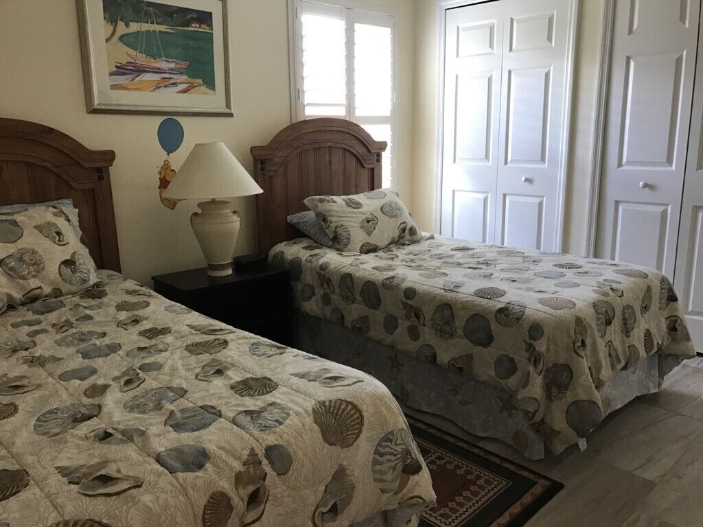 A bedroom with two beds, each with a seashell-patterned bedspread, a nightstand with a lamp, and a framed picture on the wall.