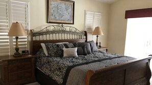 Une chambre à coucher avec un lit en bois, deux tables de chevet avec des lampes, une petite table et un tableau encadré au mur.
