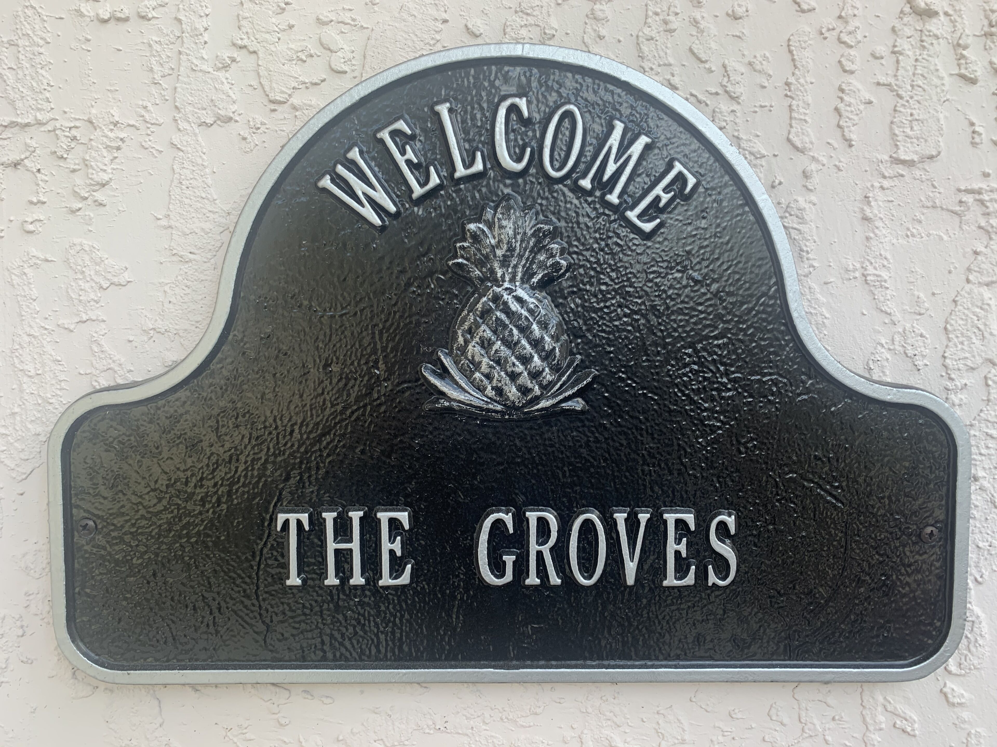 Un letrero de bienvenida con un emblema de piña y el texto "THE GROVES".