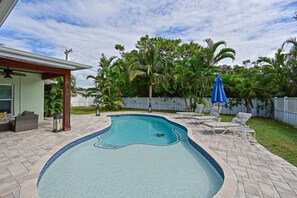 A swimming pool with a curved edge, surrounded by a brick patio. There are lounge chairs and a blue umbrella. - Tropical Luxury Escape – Heated Pool, Pets OK, IMG (Bradenton)