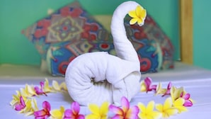 Una toalla con forma de cisne sobre una cama con almohadas y flores coloridas.