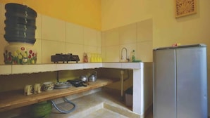 Una cocina con un lavamanos, un refrigerador y una estantería de madera con utensilios de cocina.