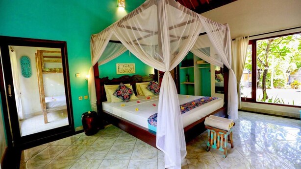 Una habitación con una cama con dosel, un taburete pequeño, un espejo y una puerta.