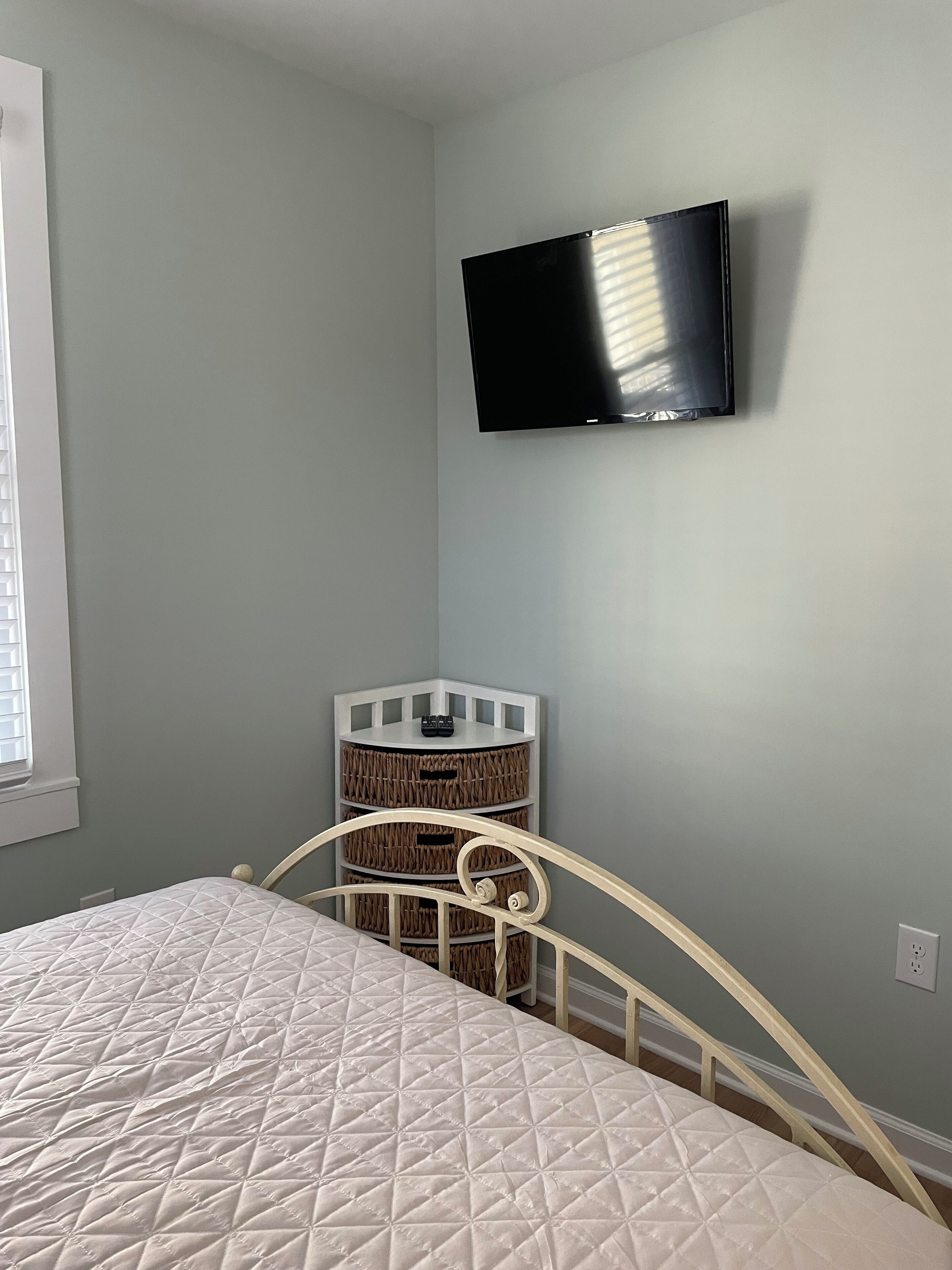 A bedroom with a bed, a TV mounted on the wall, and a storage unit with baskets.