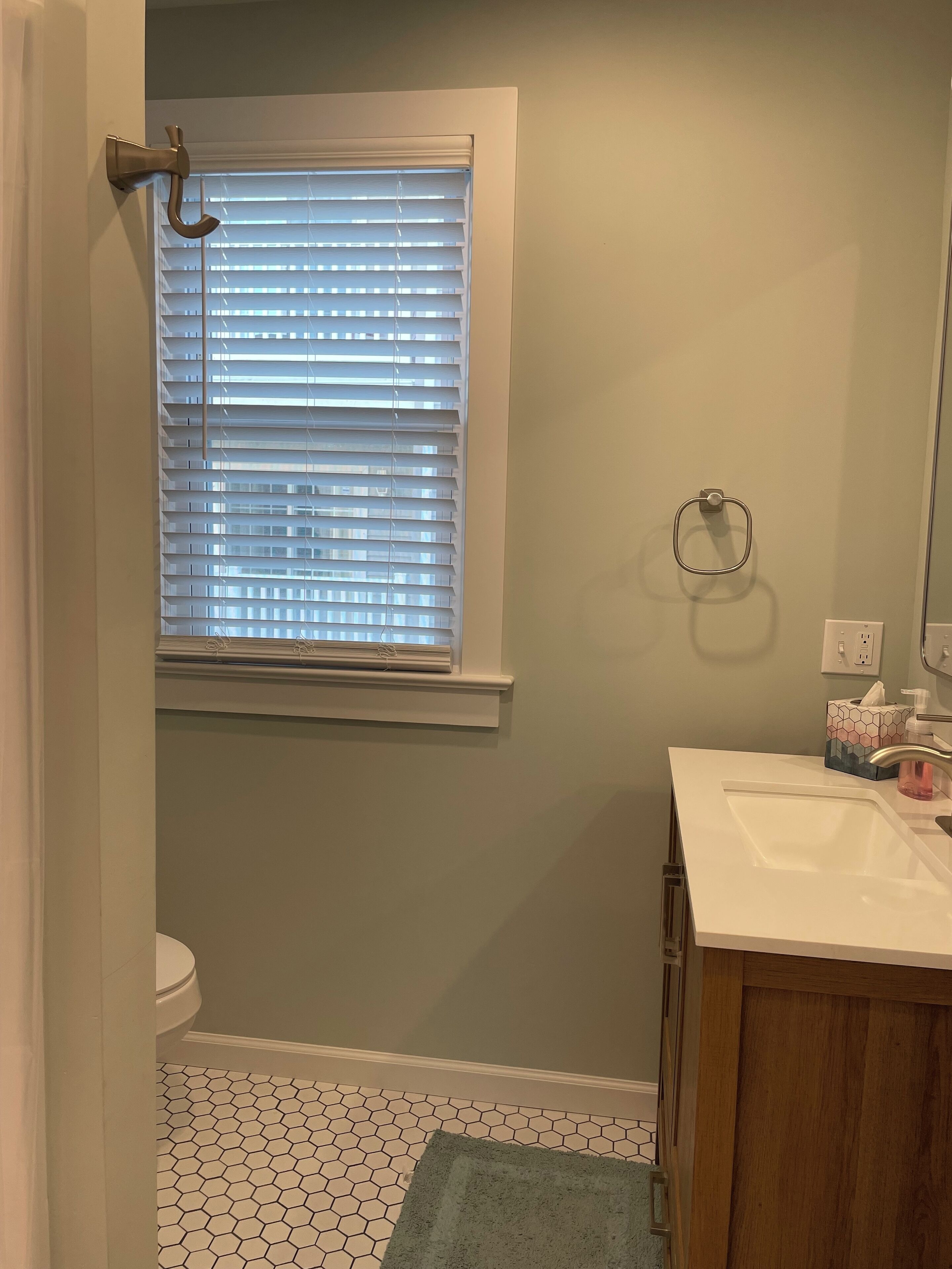 A bathroom with a toilet, a sink, a window with blinds, and a towel rack.