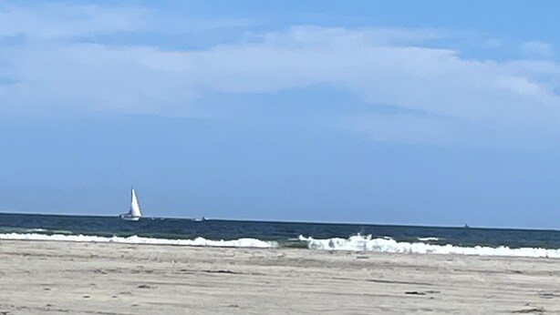 Une plage avec un voilier à l’horizon et un ciel dégagé.
