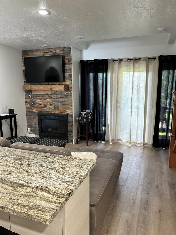Una sala moderna con chimenea de piedra, televisor de pantalla plana, un sofá seccional grande y una zona de comedor con encimera de granito.