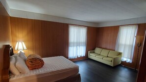 Quarto de hotel com cama, sofá e duas janelas com cortinas.
