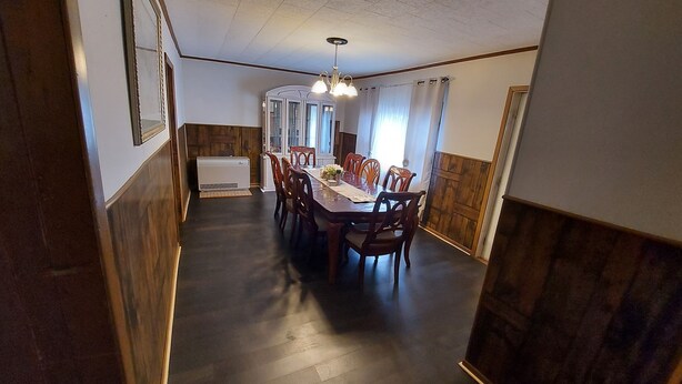 Uma sala de jantar com uma mesa comprida, cadeiras de madeira e um ventilador de teto.
