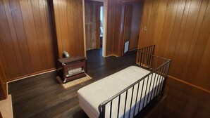 Quarto com painéis de madeira, berço, escrivaninha de madeira e luminária no teto.
