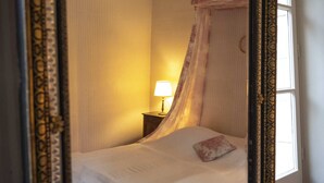 Una habitación con cama, mesita de noche, lámpara y ventana.