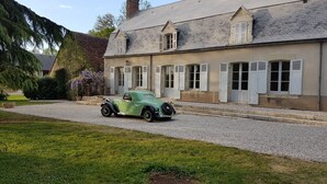 Un coche verde antiguo estacionado frente a un edificio con múltiples ventanas y persianas.