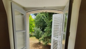Una habitación con ventana que da a un jardín, un radiador debajo de la ventana y suelo de madera.