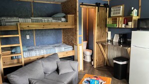 Una habitación compacta con literas, un sofá, una pequeña cocina con microondas y un cesto de basura.