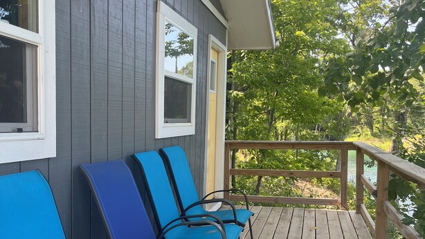 Una terraza de madera con sillas azules y barandilla, con vistas a un paisaje natural.