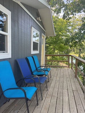 A wooden deck with blue chairs and a railing, overlooking a natural landscape. - Private Waterfront Cabins (Bussey)