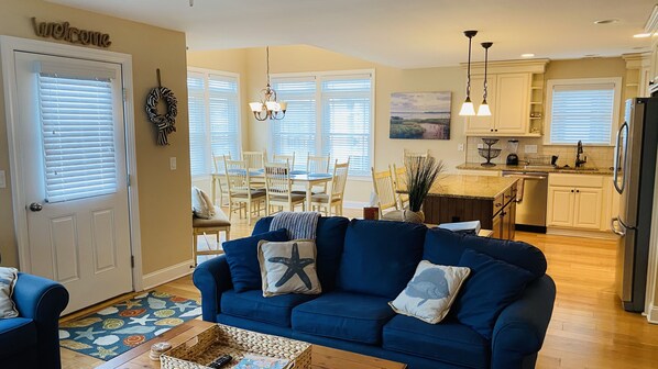 A living room with a blue sofa, a dining area with a table and chairs, and a kitchen with a refrigerator and countertop appliances. - 9th & Wesley Ave - Downtown fantastic location (Ocean City)
