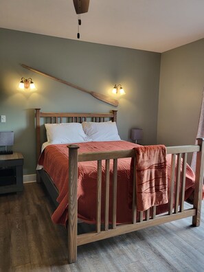 A bedroom with a wooden bed, two wall-mounted lamps, a nightstand, and a wooden floor. - Downtown by the river (Hesperia)