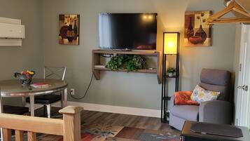 A living room with a flat-screen TV, a dining table with chairs, a sofa, and a small black side table.