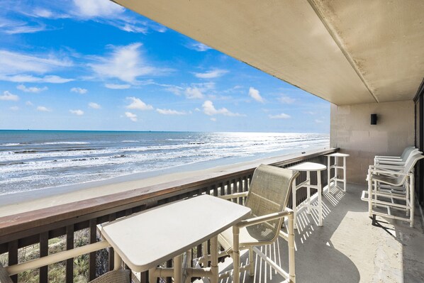 Un balcon offrant une vue sur l’océan, avec des fauteuils et une table en osier blanc.