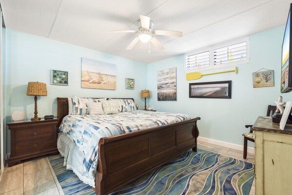 A bedroom with a bed, nightstands, a ceiling fan, and artwork on the walls.