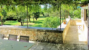 Muro de piedra con un banco y una mesa, con vistas a un jardín con árboles y césped.