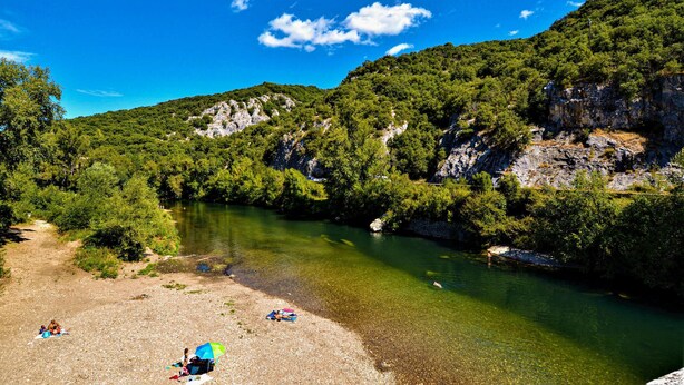 Un río de aguas claras rodeado de colinas verdes y riscos rocosos.