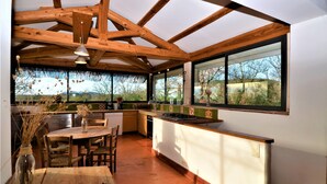Una cocina rústica con vigas de madera, un comedor con mesa y sillas, y amplias ventanas que ofrecen vistas al exterior.