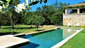 Una piscina rectangular con agua azul cristalina, rodeada por un muro de piedra y una zona verde con algunos árboles.