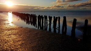 A beach with a wooden pier extending into calm waters, reflecting the sunset.