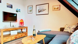 A living room with a TV, a lava lamp, a bottle of champagne, and a sofa.